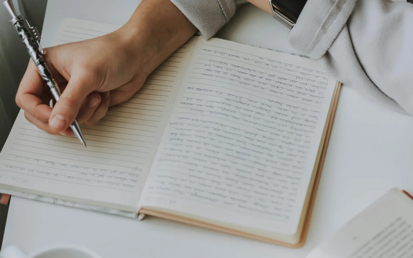 Writer drafting in a notebook beside coffee and open books.